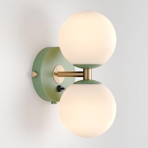 May include: A green wall-mounted light fixture with two white glass globes. The fixture has a brass arm connecting the globes.