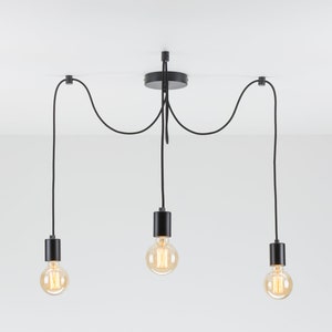 May include: Black pendant light fixture with three hanging bulbs. The fixture has a black metal canopy and black cords.