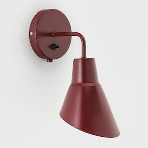 Peut inclure: Un luminaire mural rouge avec un abat-jour en forme de cône. La lumière a un simple interrupteur marche/arrêt.