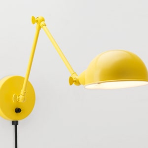 May include: A bright yellow wall-mounted lamp with an adjustable arm and a rounded lampshade. The lamp is attached to a circular base and has a black power cord. The design is modern and minimalist.