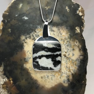 May include: A silver pendant necklace with a square black and white stone. The stone has a marbled pattern.