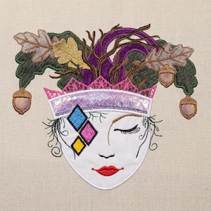 May include: Embroidered face design with a white base, closed eye, and red lips. The design features a crown with pink and iridescent accents, and is adorned with leaves, acorns, and purple branches. The face has three colourful diamond shapes.