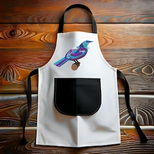 May include: White kitchen apron with a black pocket and a colourful bird design. The bird is perched on a branch and has blue, purple and green feathers.