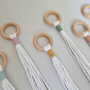 May include: Six wooden plant hangers with white cotton cords. Each has a natural wood ring and a band of coloured yarn in pink, green, yellow, and orange. These hangers are designed for indoor use and are ideal for displaying plants.