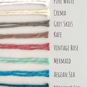 Puede incluir: Una colección de ocho cordones de algodón de diferentes colores, cada uno con una etiqueta que indica su nombre de color: Blanco puro, Crema, Cielos grises, Kaffe, Rosa vintage, Sirena, Mar Egeo y Cielo nocturno.