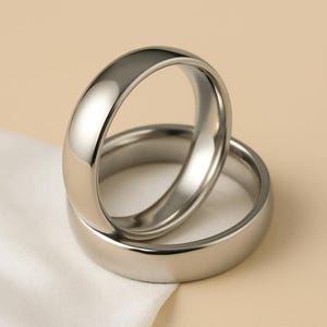 以下が含まれることがあります： 2つの磨かれたシルバーカラーのリングが重ねられています。リングは滑らかで丸みを帯びたデザインで、光沢のある反射面を持っています。リングはニュートラルな背景に配置されています。