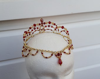 May include: A gold and red beaded crown with a teardrop-shaped pendant. The crown is made of small beads and has a delicate design.
