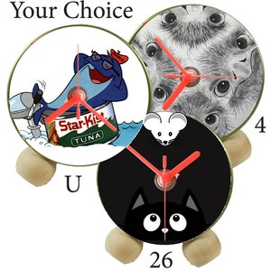 May include: Three different designs for a clock with a wooden base. The first clock features a cartoon tuna on a can of Star-Kist tuna. The second clock features a black and white image of an ostrich. The third clock features a black cat with large eyes on a black background.