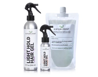 Puede incluir: Dos botellas plateadas de gel para el cabello de fijación ligera "a simple planet", una de 9 onzas líquidas y la otra de 2,7 onzas líquidas, con una bolsa de plástico transparente del mismo producto en el fondo. Las botellas tienen una boquilla de pulverización negra y el texto "a simple planet" está impreso en las botellas.