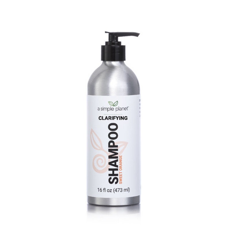 May include: A silver bottle of clarifying shampoo with a black pump top. The bottle is labeled "a simple planet" and "Clarifying Shampoo Sweet Orange" with a pink and orange graphic. The bottle contains 16 fl oz (473 ml).