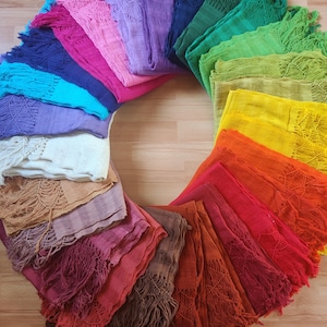 Può includere: Una vibrante collezione di sciarpe colorate con frange disposte a cerchio. Le sciarpe presentano un'ampia gamma di tonalità, tra cui rosa, blu, verdi, gialli, arancioni e rossi. Ogni sciarpa ha un design a trama aperta.