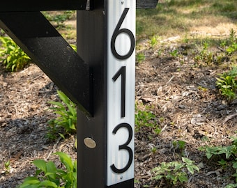 May include: A black and white house number sign with the numbers 613 on a white background. The sign is attached to a black wooden post.