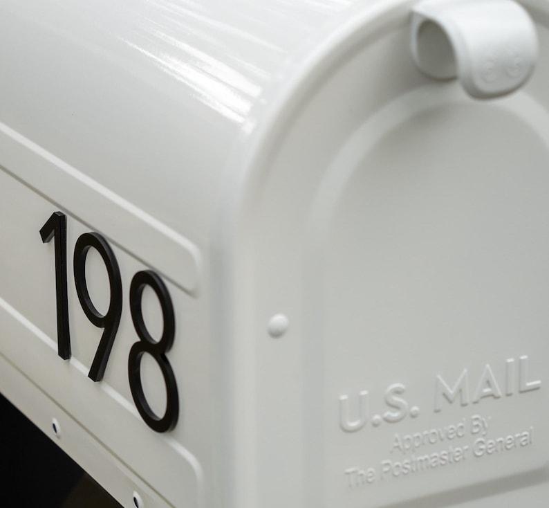 May include: A glossy white metal mailbox featuring the black house numbers 198 on the side. The front door panel is embossed with the text U.S. MAIL Approved By The Postmaster General and includes a white handle at the top for opening the lid.