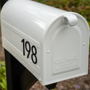 May include: A white metal mailbox featuring the black house number 198 on the side. The front door is embossed with the text U.S. MAIL and Approved By The Postmaster General. The mailbox is mounted on a black post and has a curved top design.