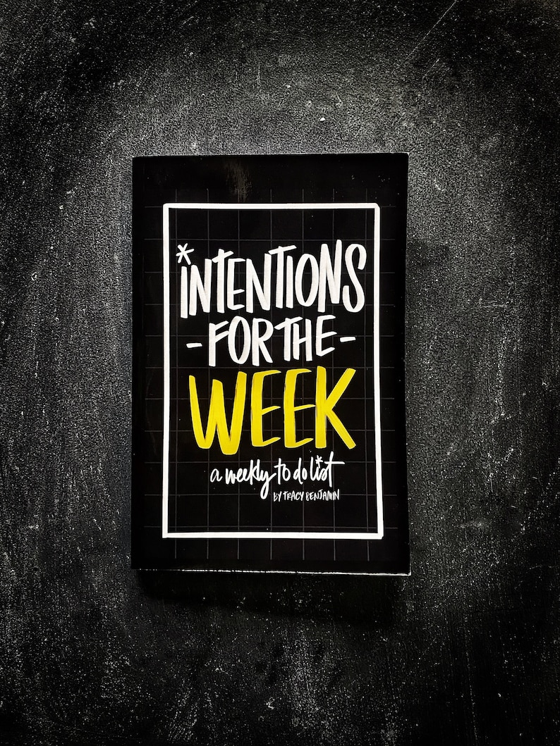 May include: A black and white book with a yellow title that reads "Intentions for the Week: a weekly to do list by Tracy Benjamin".