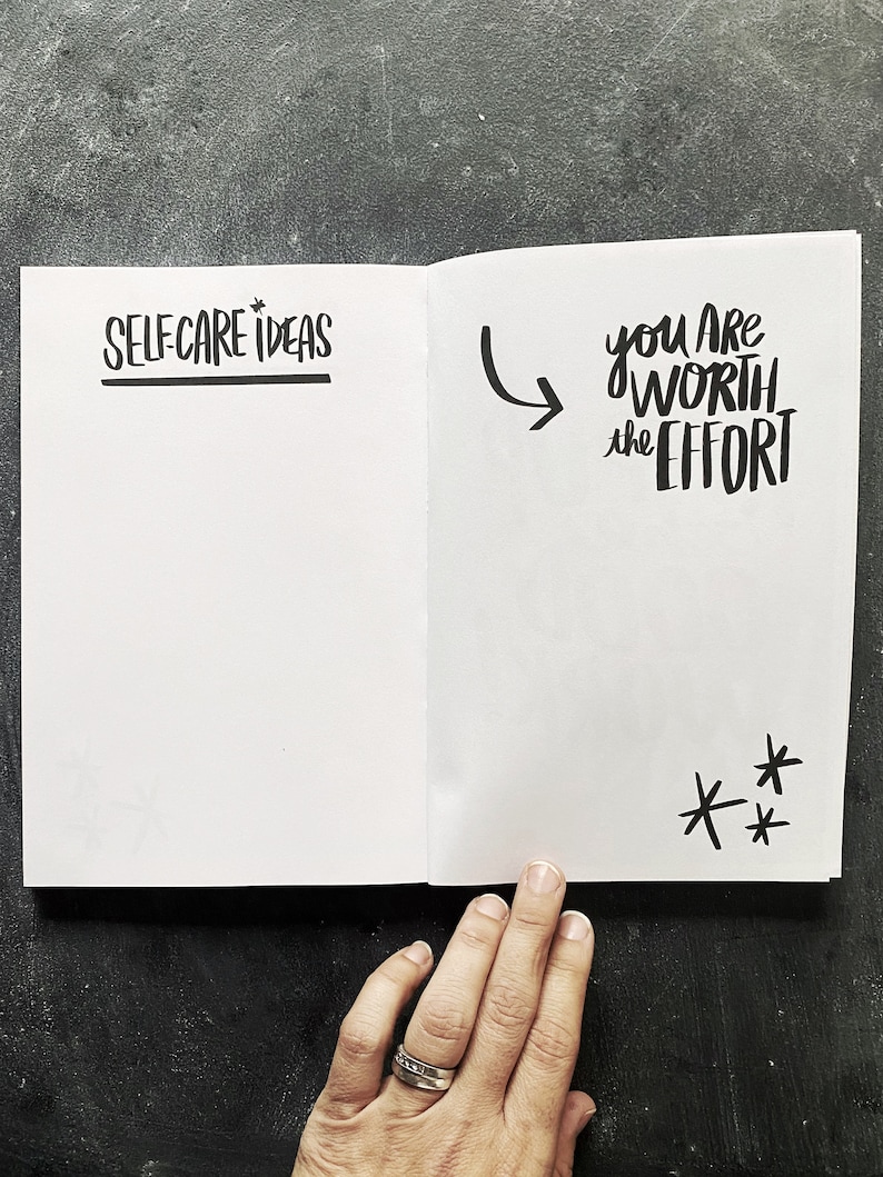 May include: An open notebook with the words "SELF-CARE IDEAS" on the left page and "YOU ARE WORTH THE EFFORT" on the right page. The right page also has three stars drawn at the bottom.