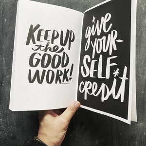 May include: Open book with black pages and white text. The left page says "Keep up the good work!" and the right page says "Give your self credit."