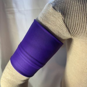 May include: Purple arm band made of a soft, stretchy fabric. The band is worn on the upper arm.