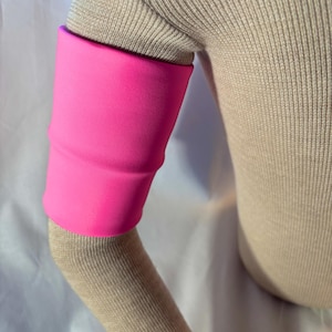 May include: A bright pink arm sleeve, made of a soft material, is worn on the arm. The sleeve is a solid color and covers the arm from the elbow to the upper arm. The sleeve is a vibrant, eye-catching accessory.