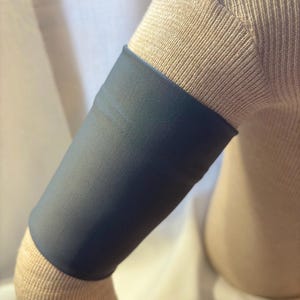 May include: A gray arm sleeve made of a soft, stretchy fabric. The sleeve is worn on the upper arm and extends to the elbow.