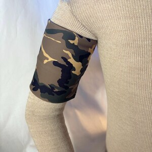 May include: Camouflage arm sleeve in shades of brown, green, and tan. The sleeve is worn on the arm, covering the forearm. The fabric has a military-style pattern. The sleeve is made of a soft, flexible material.