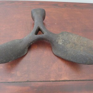 May include: A vintage cast iron shoe last with a triangular shape and two rounded ends. The last is worn and has a dark brown patina.
