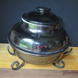 May include: Black ceramic crock with a lid and a metal stand. The crock has a shiny, almost metallic finish.