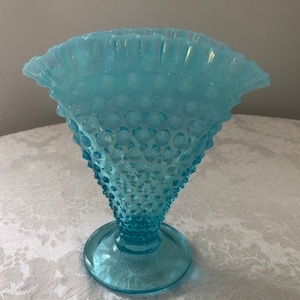 May include: A light blue glass vase with a textured, bubbled surface and a ruffled top. The vase has a wide base and a narrow neck.