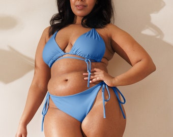 Könnte beinhalten: Ein hellblaues Bikini-Set. Das Oberteil ist im Triangel-Stil mit verstellbaren Trägern, und das Unterteil ist ein klassischer Schnitt mit Bindebändern an den Seiten. Die Bademode ist aus einem glatten, einfarbigen Stoff gefertigt. Das Model steht vor einem neutralen Hintergrund.