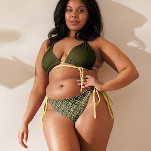 Könnte beinhalten: Olivgrüner Bikini mit geometrisch gemusterter Hose und einfarbigem Oberteil. Das Bikini-Oberteil hat gelbe Paspeln und Bindebänder, und die Hose hat gelbe Bindebänder. Die Frau steht vor einer neutralen Wand.