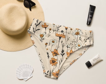 Può includere: Un paio di slip bikini a vita alta con stampa floreale con margherite bianche e fiori arancioni su sfondo crema.
