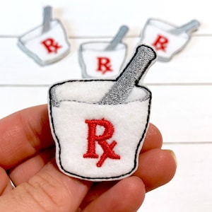 May include: Three white felt embroidered patches with a red "Rx" and a silver stirring stick. The patches are shaped like a medicine cup.