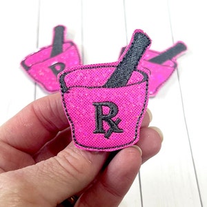 May include: Pink glitter iron-on patch with a mortar and pestle design and the letter "R" in the center.
