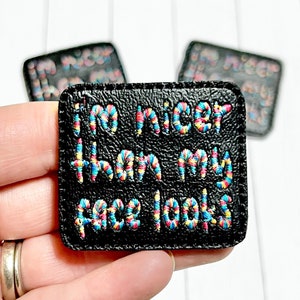 May include: A black leather patch with colorful embroidery that reads "I'm nicer than my face looks."
