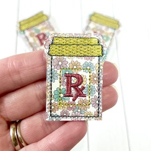 May include: A small, embroidered patch featuring a floral design with a yellow lid and the letter "R" in red. The patch is perfect for adding a touch of whimsy to clothing, bags, or other accessories.