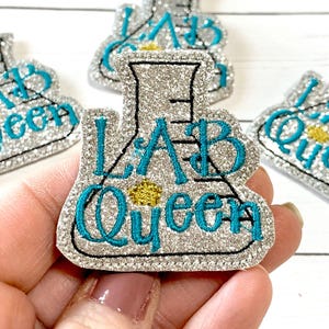 May include: Silver glitter iron-on patch with a turquoise blue embroidered beaker and the text "Lab Queen".