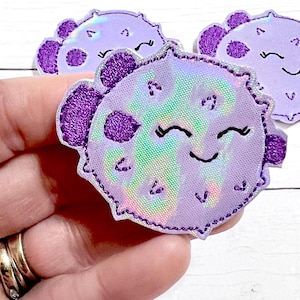May include: Three purple and iridescent embroidered iron-on patches shaped like pufferfish with smiling faces.