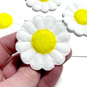 May include: Four white felt daisy flowers with yellow centers. The daisies are approximately 2 inches in diameter.