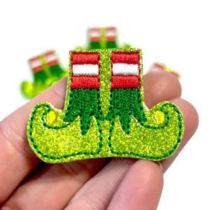 May include: Green glitter elf shoes with red and white striped cuffs. The shoes have a pointed toe and a curled up heel.