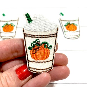 May include: Three embroidered iron-on patches featuring a pumpkin spice latte with whipped cream and a straw. The latte is in a white cup with a brown rim and a brown lid. The pumpkin is orange with a green stem and leaves.