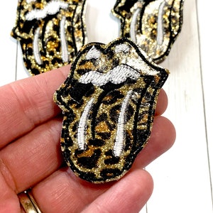 May include: Three gold and black glitter iron-on patches in the shape of a tongue with a leopard print design.