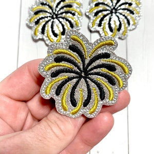 May include: Three silver glitter iron-on patches with black and gold embroidery of a firework design.