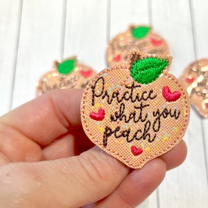 May include: Peach-shaped embroidered iron-on patch with the text "Practice what you peach" in black cursive font. The peach is pink with glitter and has a green leaf and red hearts.