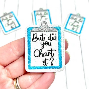 Peut inclure: Patch thermocollante blanche avec bordure bleue et argentée. Le patch est en forme de presse-papiers et dit "But did you chart it?" en écriture cursive noire.