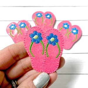 May include: Four pink glitter flip-flop patches with blue and green embroidered flowers.