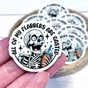 May include: A circular sticker with a skeleton illustration holding a coffee. The text "ALL OF MY FLABBERS ARE GASTED" is arranged around the skeleton. The sticker has a white background with star accents. Other stickers are visible.