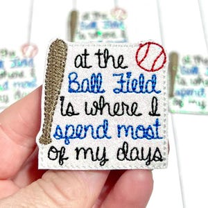 May include: A white baseball-themed patch with the text "at the Ball Field is where I spend most of my days" in black and blue stitching. A baseball bat and ball are also embroidered on the patch.