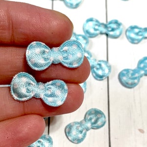 May include: A collection of light blue satin bows with white polka dots. The bows are approximately 1 inch in diameter and are perfect for adding a touch of whimsy to crafts, gifts, and clothing.