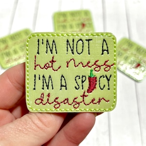 May include: A green embroidered patch with the text "I'm not a hot mess I'm a spicy disaster" and a red chili pepper graphic.