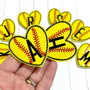 May include: A set of nine yellow heart-shaped softball patches with black letters, each letter representing a different letter of the alphabet. The letters are J, R, S, E, K, A, H, and M.